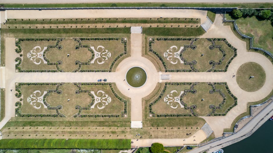 An aerial view of the historic garden at the Royal Hospital Chelsea, featuring a symmetrical layout with four ornate, geometric garden beds bordered by neatly trimmed grass and low hedges. Central to